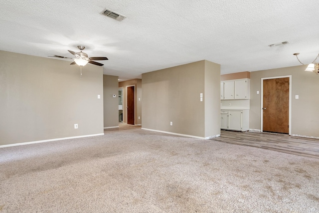 unfurnished living room with a textured ceiling, baseboards, visible vents, light colored carpet, and a ceiling fan