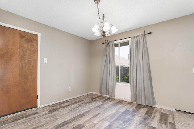 unfurnished room featuring wood finished floors, baseboards, and an inviting chandelier