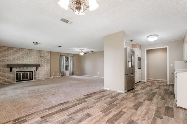 unfurnished living room with a textured ceiling, light wood finished floors, a fireplace, baseboards, and visible vents
