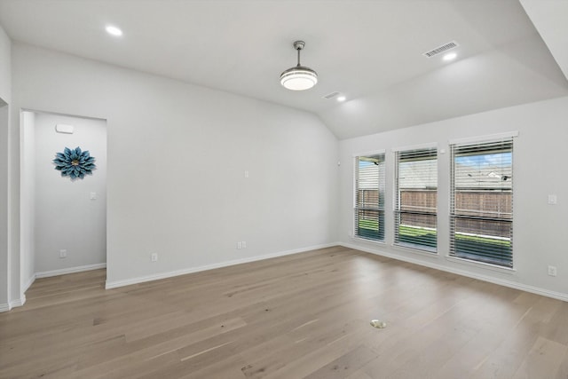 spare room featuring light wood-style flooring, vaulted ceiling, baseboards, visible vents, and recessed lighting
