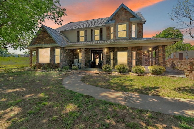 view of front facade featuring a lawn, stone siding, metal roof, and covered porch