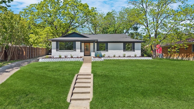 view of front facade with brick siding, fence, roof with shingles, and a front yard