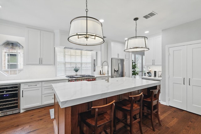 kitchen featuring beverage cooler, visible vents, decorative backsplash, a kitchen island with sink, and appliances with stainless steel finishes