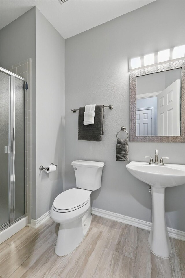 bathroom with a shower stall, toilet, wood finished floors, and baseboards