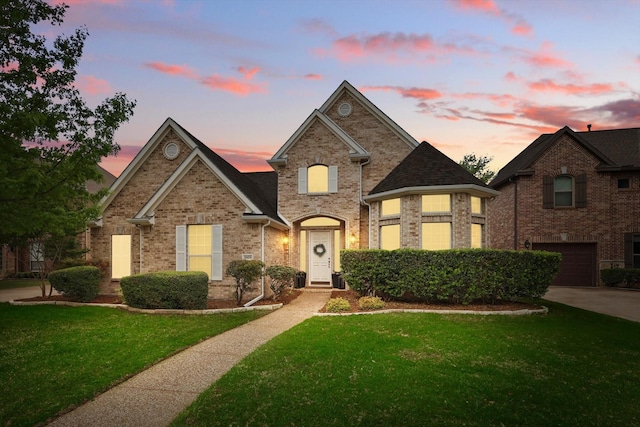 view of front of house featuring brick siding, a yard, an attached garage, and driveway