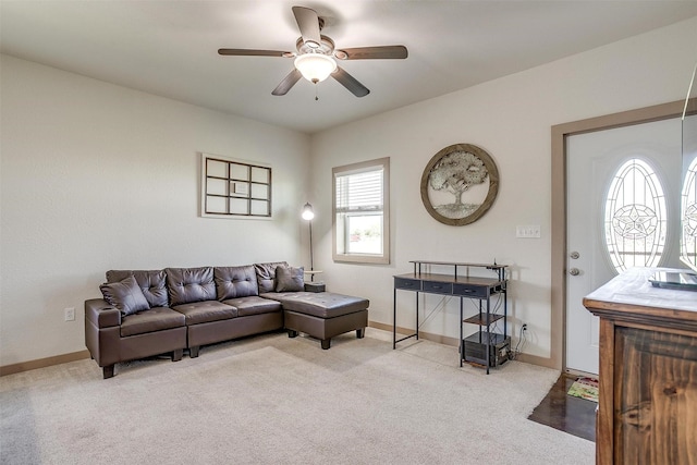 living area featuring baseboards, a ceiling fan, and light colored carpet