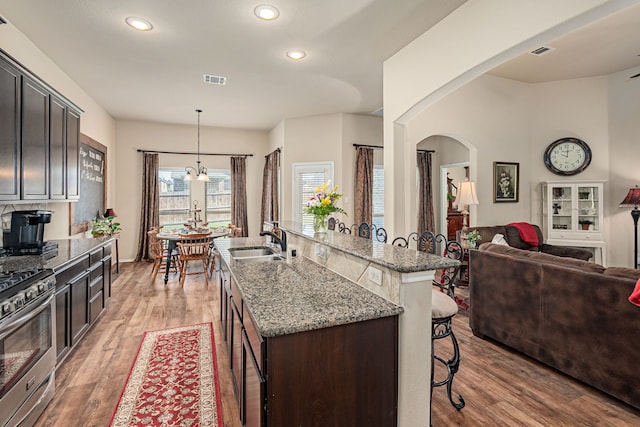 kitchen featuring a kitchen breakfast bar, a sink, stainless steel gas range, open floor plan, and light stone counters