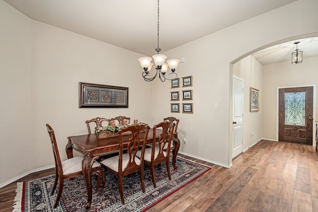 dining space featuring arched walkways, wood finished floors, baseboards, and an inviting chandelier