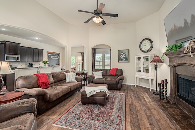 living room featuring a fireplace with flush hearth, dark wood finished floors, arched walkways, and ceiling fan