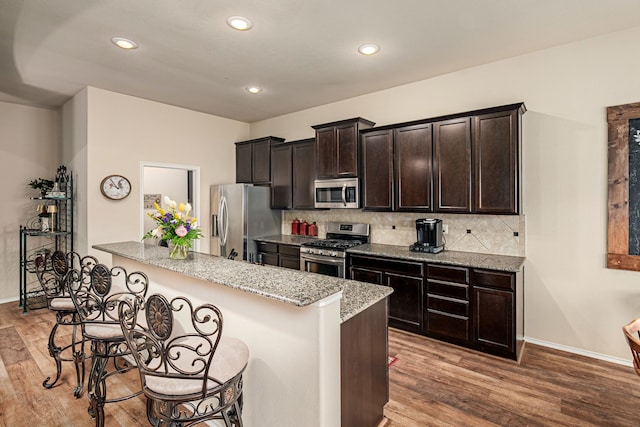 kitchen featuring tasteful backsplash, wood finished floors, stainless steel appliances, and a breakfast bar area