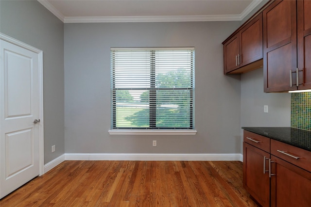 kitchen featuring dark stone countertops, crown molding, baseboards, decorative backsplash, and light wood-style flooring