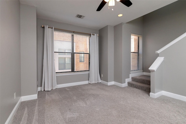 carpeted empty room featuring visible vents, baseboards, stairway, and ceiling fan
