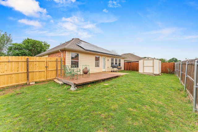 back of house with a deck, a fenced backyard, a storage unit, an outbuilding, and solar panels