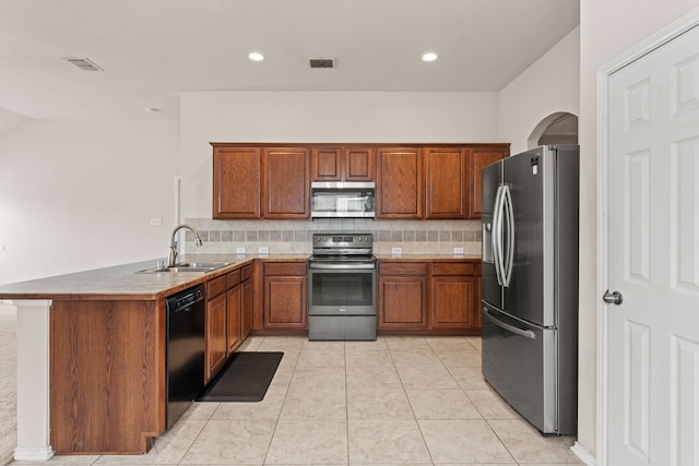kitchen featuring stainless steel appliances, brown cabinetry, a sink, and a peninsula
