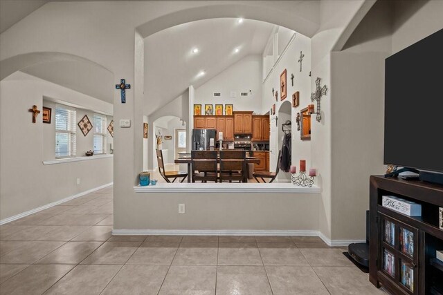 living room featuring baseboards, arched walkways, light tile patterned floors, and high vaulted ceiling