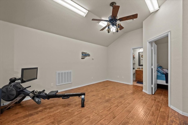 workout area featuring ceiling fan, visible vents, light wood-style flooring, and lofted ceiling