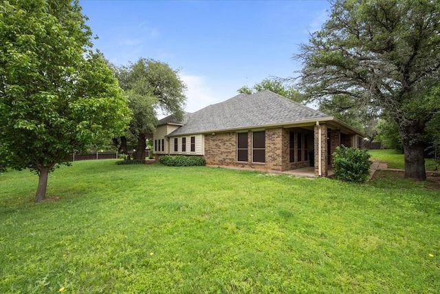 back of property with roof with shingles, a yard, and brick siding