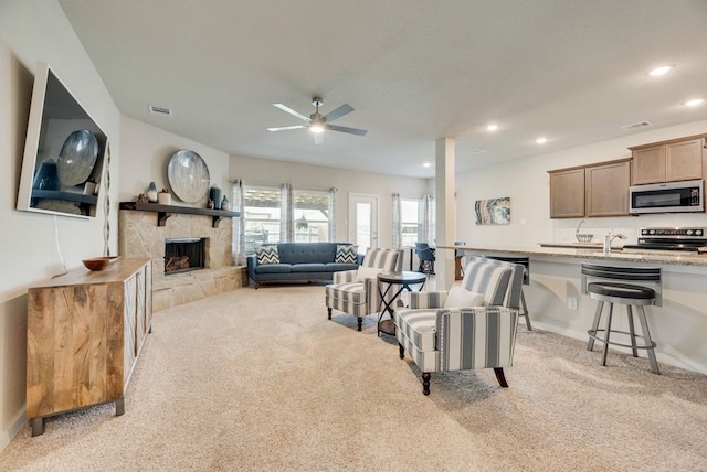 living room with a fireplace, ceiling fan, visible vents, and light carpet