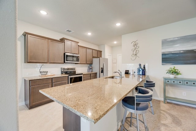 kitchen featuring light stone counters, a sink, a breakfast bar area, a peninsula, and appliances with stainless steel finishes