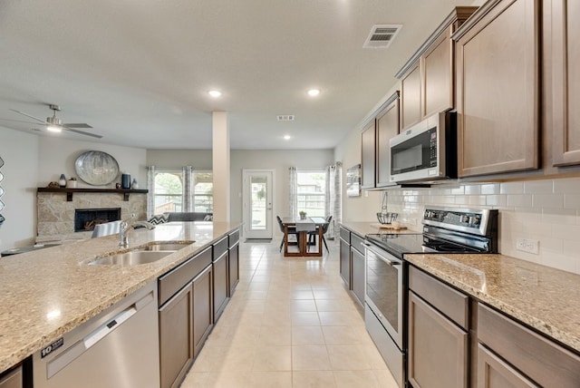 kitchen with a stone fireplace, visible vents, a sink, decorative backsplash, and appliances with stainless steel finishes