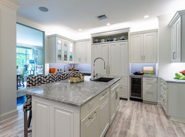 kitchen featuring a sink, a kitchen bar, backsplash, wine cooler, and visible vents