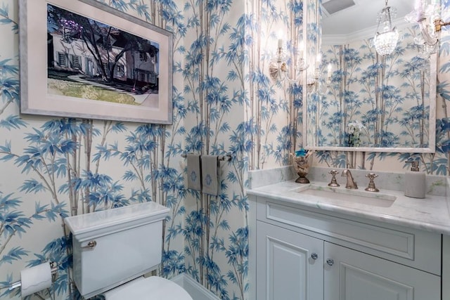 half bath featuring wallpapered walls, toilet, vanity, crown molding, and a chandelier