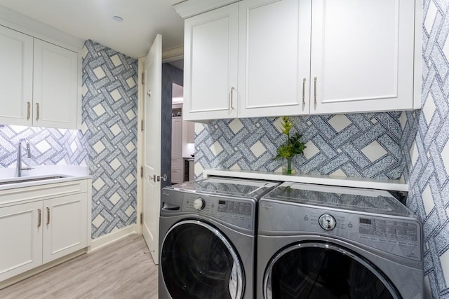 clothes washing area featuring washer and clothes dryer, cabinet space, a sink, and light wood finished floors