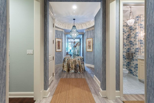 hallway with baseboards, wood finished floors, a notable chandelier, and crown molding