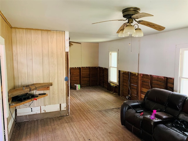 living room featuring wood-type flooring, wooden walls, and a ceiling fan