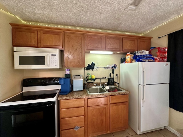 kitchen featuring brown cabinets, light tile patterned floors, a sink, white appliances, and a textured ceiling