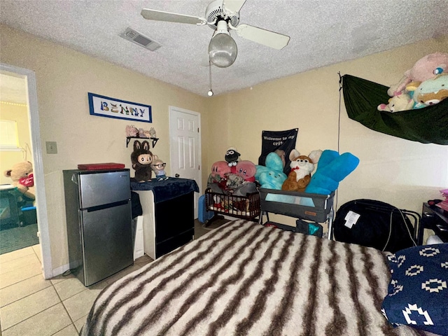 tiled bedroom featuring ceiling fan, a textured ceiling, visible vents, and freestanding refrigerator