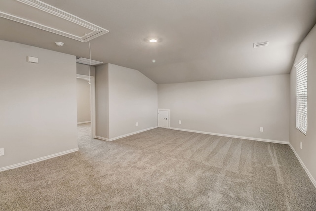 carpeted spare room featuring attic access, lofted ceiling, and baseboards