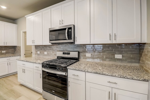 kitchen with white cabinets, light wood-style floors, backsplash, light stone counters, and appliances with stainless steel finishes