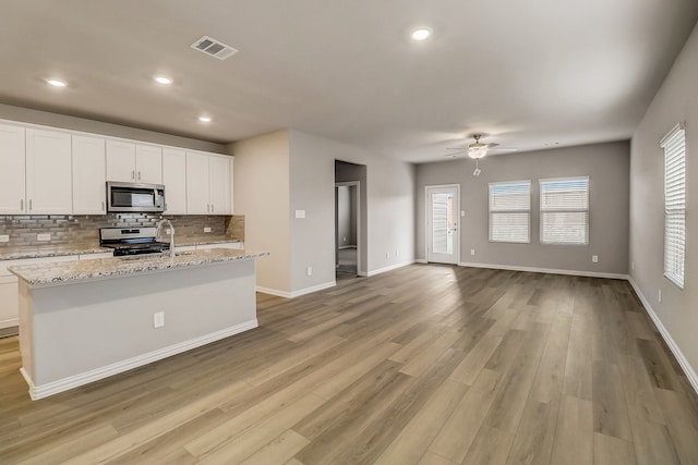 kitchen with an island with sink, stainless steel appliances, visible vents, a ceiling fan, and open floor plan