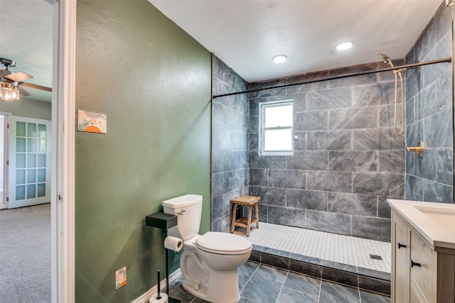 bathroom with toilet, a textured wall, vanity, and tiled shower