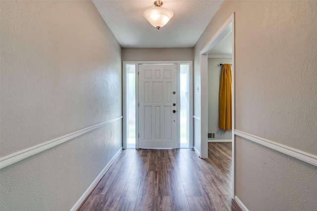 foyer with a textured wall, visible vents, baseboards, and wood finished floors