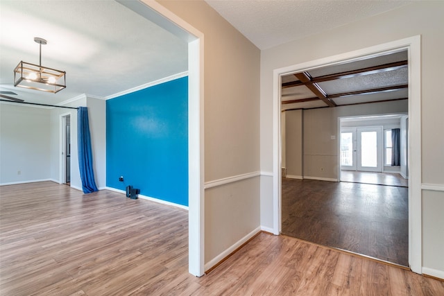 unfurnished room featuring wood finished floors, baseboards, ornamental molding, and an inviting chandelier