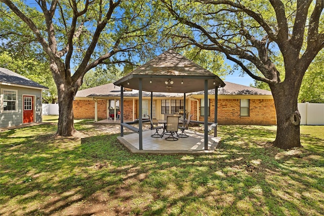 rear view of house with fence, brick siding, a yard, and a gazebo