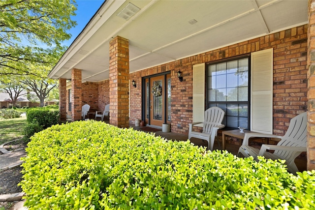 view of exterior entry featuring a porch and brick siding