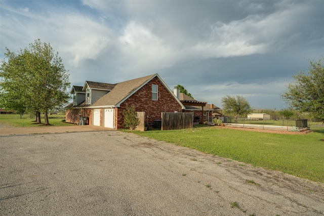 view of property exterior with fence, driveway, brick siding, and a yard