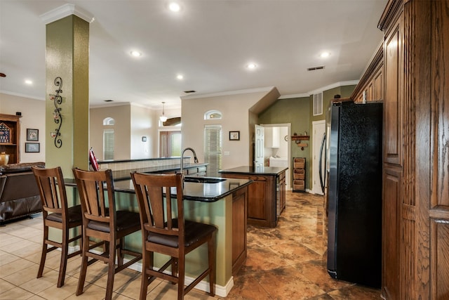 kitchen featuring dark countertops, a center island, a kitchen breakfast bar, a sink, and freestanding refrigerator