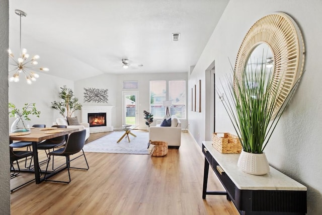 living area featuring lofted ceiling, a glass covered fireplace, visible vents, and light wood-style flooring