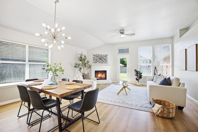 dining area with lofted ceiling, light wood finished floors, baseboards, a fireplace, and ceiling fan with notable chandelier