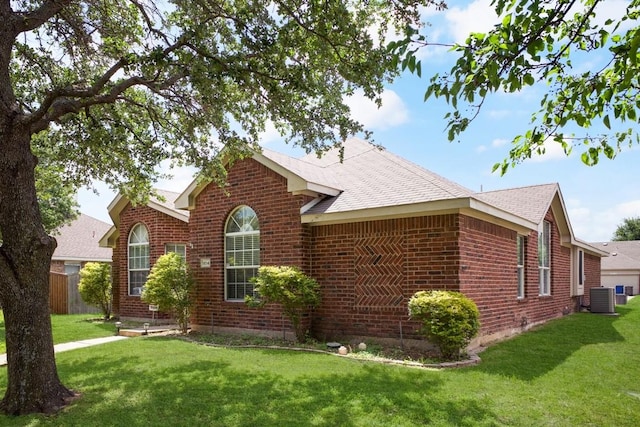 view of front of house featuring brick siding, cooling unit, a shingled roof, and a front lawn