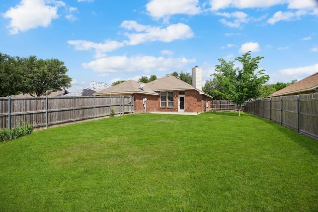 back of house featuring a fenced backyard, a chimney, brick siding, and a yard