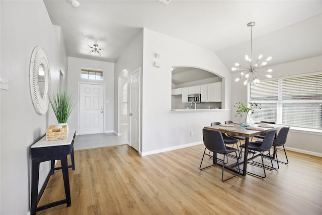 dining area with arched walkways, vaulted ceiling, baseboards, a notable chandelier, and light wood-style floors