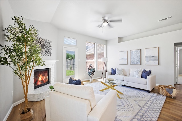 living room with baseboards, visible vents, a ceiling fan, wood finished floors, and a fireplace