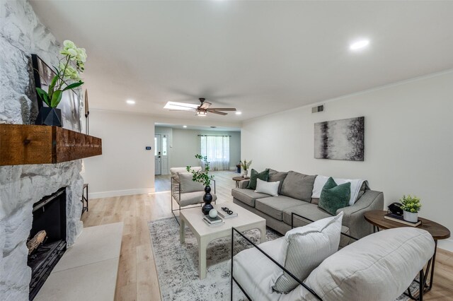 living room with a stone fireplace, light wood-style floors, ornamental molding, recessed lighting, and a ceiling fan