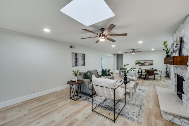 living area with a fireplace, ceiling fan, recessed lighting, light wood-style flooring, and a skylight