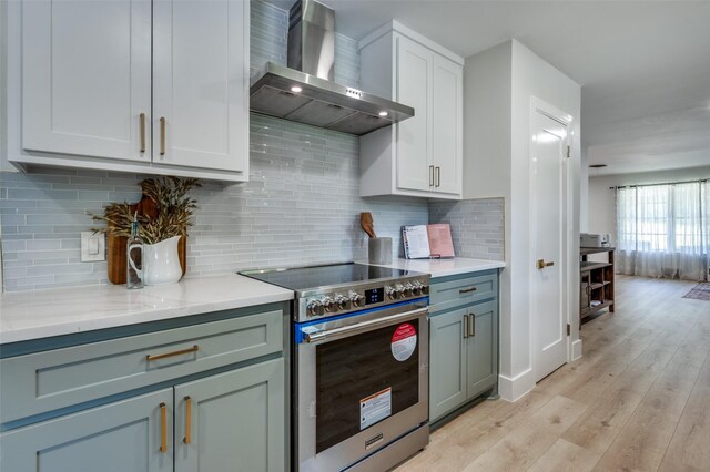 kitchen with high end stove, wall chimney exhaust hood, light wood-style flooring, and tasteful backsplash